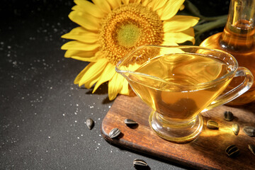 Wooden board with gravy boat of sunflower oil and seeds on black background