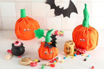 Paper pumpkins for Halloween and tasty candies on light background