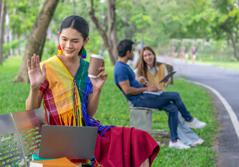 attractive transgender woman in lgbt colorful rainbow clothes sitting on bench in the park,relaxing,surfing internet on laptop,communicate with friends or family