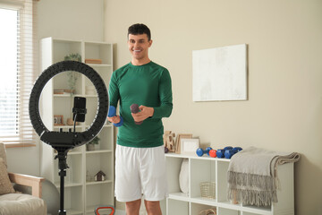 Sporty happy male blogger with dumbbells recording video at home