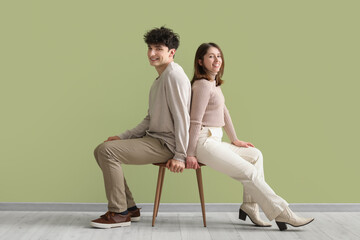 Young beautiful couple in stylish clothes sitting on one chair on green background