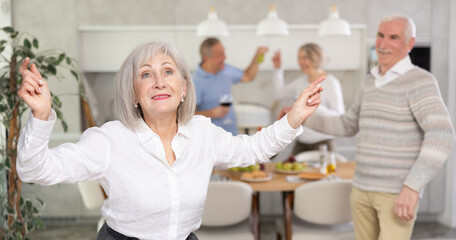 Two married couples pensioners dance during holiday, have fun, move and jump in dining room. Family event is held with fun music and dancing