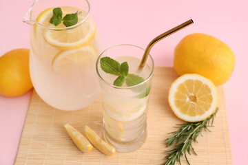 Glass and jug of fresh lemonade with mint on pink background