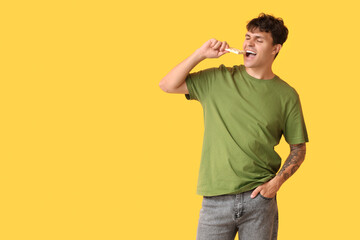 Handsome young man eating sweet white chocolate on yellow background