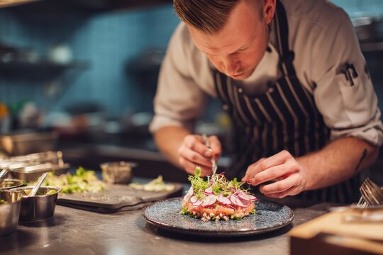 Focused male chef meticulously plates a vibrant seafood dish, showcasing culinary artistry and precision.
