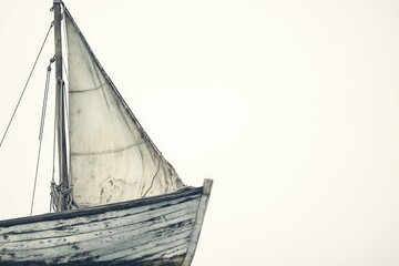 Fototapeta premium An old, weathered sailboat with a large sail stands out against a bright, minimalist background in vintage style.