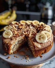 Rich banana cake with caramel drizzle and nuts, topped with a slice of banana, served on a round plate.