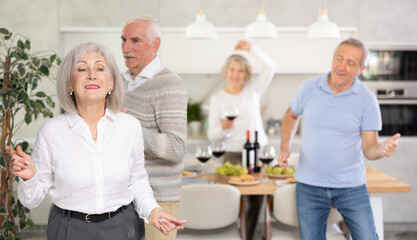 Elderly energetic woman dancing with friends in kitchen