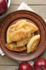 Delicious fried pyrizhky (stuffed pies) with apples on wooden table, flat lay