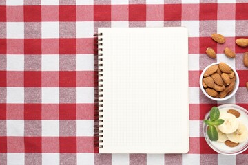 Blank recipe book, banana dessert and almonds on checkered tablecloth, top view. Mockup for design