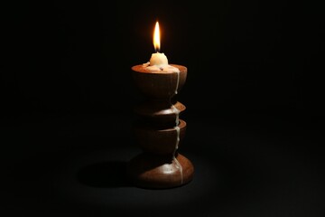 Burning candle in candlestick on black background