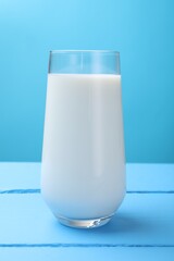 Fresh milk in glass on light blue wooden table, closeup