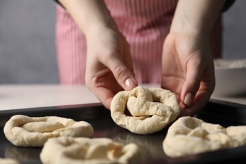 Woman putting salt onto raw pretzels at white table, closeup