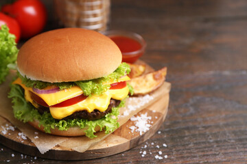 Tasty cheeseburger with potato wedges on wooden table, closeup. Space for text