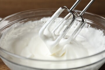 Hand mixer with whisks and bowl of whipped cream on table, closeup