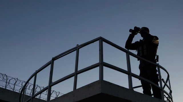 Security guard observing with binoculars on watchtower