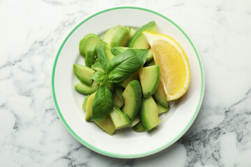 Tasty ripe green avocado, basil and lemon on white marble table, top view