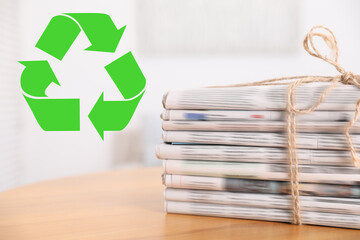 Recycling symbol and stack of tied newspapers on wooden table, closeup. Eco-friendly lifestyle,...