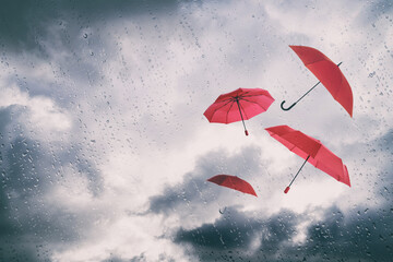 Red umbrellas flying in cloudy sky, view through wet window. Stormy weather