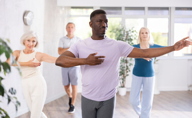Positive interested adult african american man practicing slow partner dance movements during group...