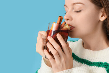 Beautiful young woman drinking hot mulled wine on blue background, closeup