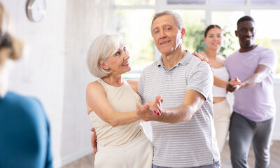 Fototapeta premium Mature male novice student of fitness studio practices paired Latin American rumba dance with elderly lady. Active hobby, movements to music, healthy lifestyle concept.