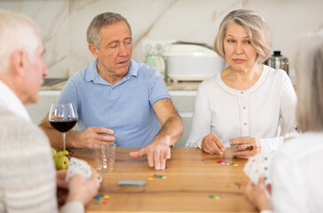 Couples of elderly women and men playing board game poker in kitchen