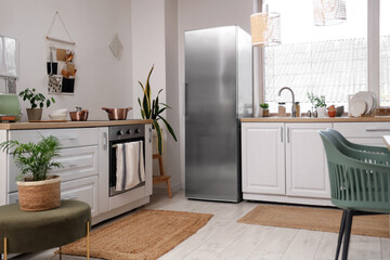 Interior of stylish kitchen with white counters, houseplants and modern refrigerator