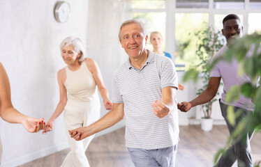 Senior europian man is engaged in modern dance class with group friends of different age and learn...
