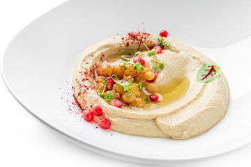 Creamy hummus on plate, garnished with chickpeas, pomegranate seeds and fresh herbs isolated on white background. Healthy food, vegetarian diet, close up, top view