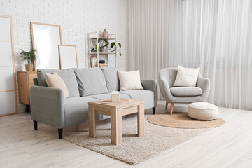 Cozy sofa, armchair, coffee table and blank posters near white brick wall in living room