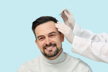 Young man receiving injection for hair growth on blue background, closeup