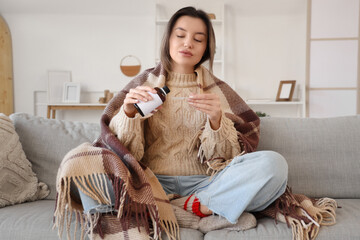 Sick young woman with plaid pouring cough syrup into spoon at home