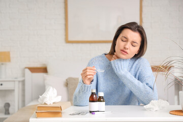 Sick young woman taking cough syrup at table in bedroom