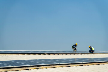 Two engineers install solar panels on a rooftop, wearing safety gear and helmets. The scene...