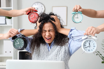 Stressed African-American businesswoman and hands with alarm clocks in office. Time management...