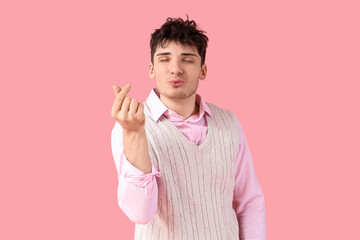 Handsome young man making heart gesture and blowing kiss on pink background