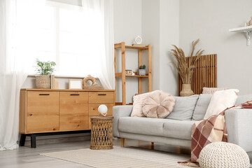 Interior of living room with chest of drawers and comfortable grey sofa near white wall