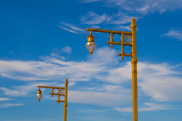 Golden street lamps against blue sky with clouds create charming urban scene. elegant design adds...