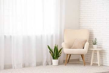 Armchair with table and plants on carpet near light curtain in room