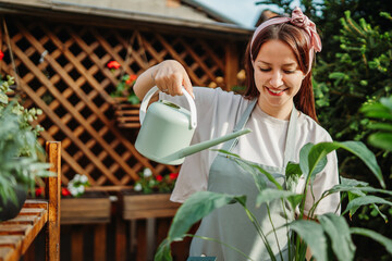 Young woman taking care of plants with water can and mister	
