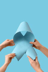Hands with blue ribbon on color background. Cancer awareness concept