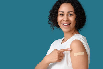 Young African-American woman pointing at applied medical patch after vaccination on blue...