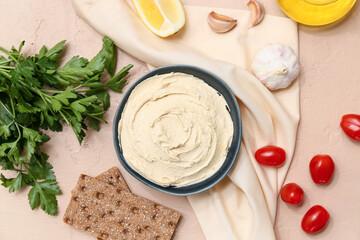 Bowl of tasty hummus with ingredients, crackers and napkin on beige grunge background