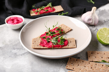 Plate with crispbreads, tasty beetroot hummus and microgreen on grunge background