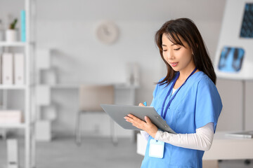 Female Asian doctor writing on clipboard in clinic