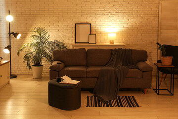 Interior of night living room with sofa, pouf, glowing lamps and houseplants