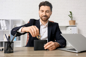 Handsome businessman putting bitcoin into wallet at table in office