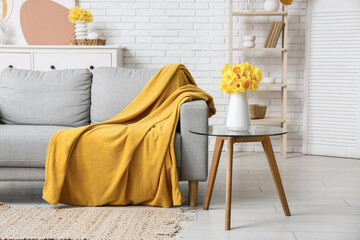 Cozy sofa with dresser, coffee table and narcissus flowers against white brick wall in living room