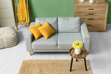 Cozy sofa with dresser, coffee table and narcissus flowers against green wall in living room